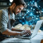 Baker in apron at stainless-steel table using a laptop beside a commercial mixer, subtle blue light trails symbolizing AI, blurred bakery racks and ovens in the background.